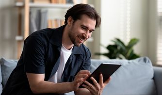 La experiencia del usuario en el entorno digital Hombre sonriente utilizando una tablet en el sofá