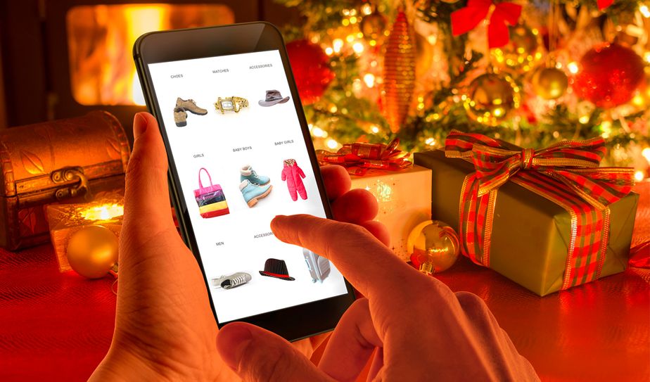 Mano usando un móvil para comprar en línea junto a regalos de Navidad