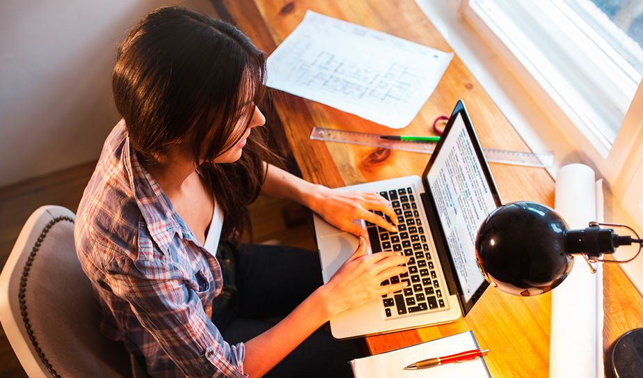 Mujer escribiendo en laptop sobre un escritorio con planos y lámpara