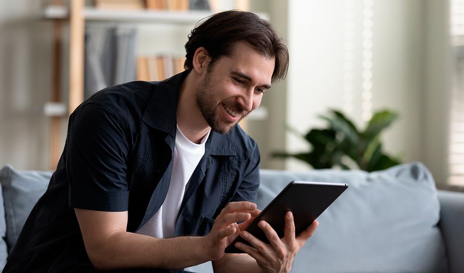 La experiencia del usuario en el entorno digital Hombre sonriente utilizando una tablet en el sofá